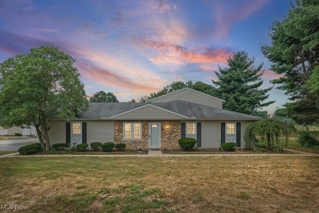 Ranch-style home with a front yard, stone siding, and a shingled roof