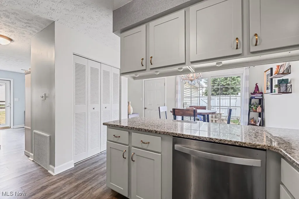 Kitchen featuring gray cabinetry, dishwasher, a textured ceiling, dark wood-type flooring, and light stone counters