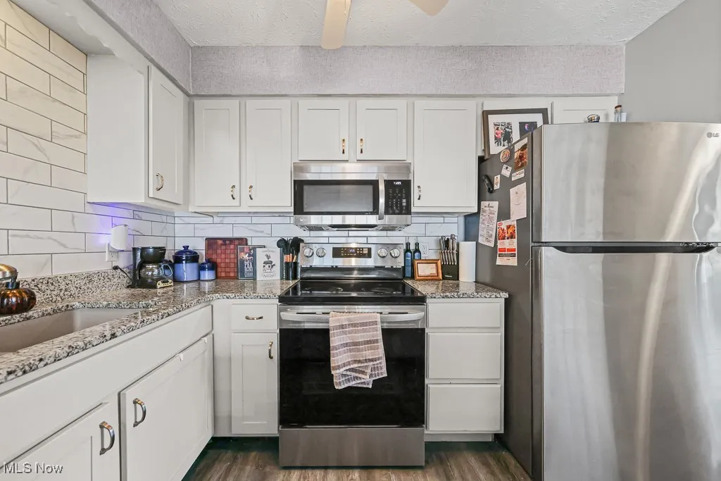 Kitchen with stainless steel appliances, white cabinets, light stone countertops, decorative backsplash, and a textured ceiling