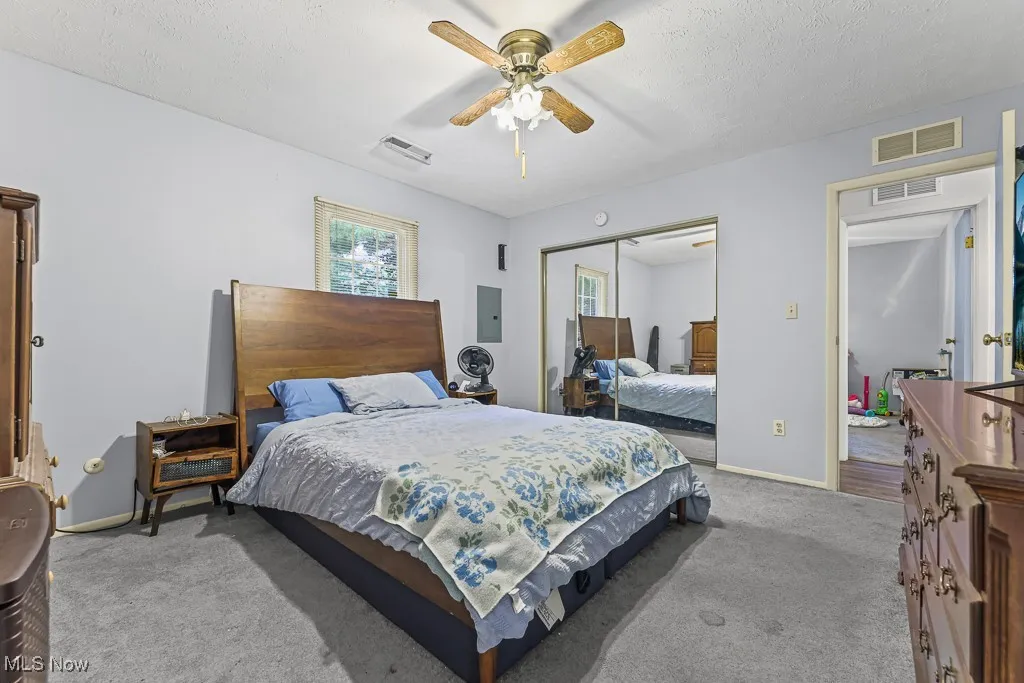 Carpeted bedroom featuring ceiling fan, a closet, electric panel, and a textured ceiling