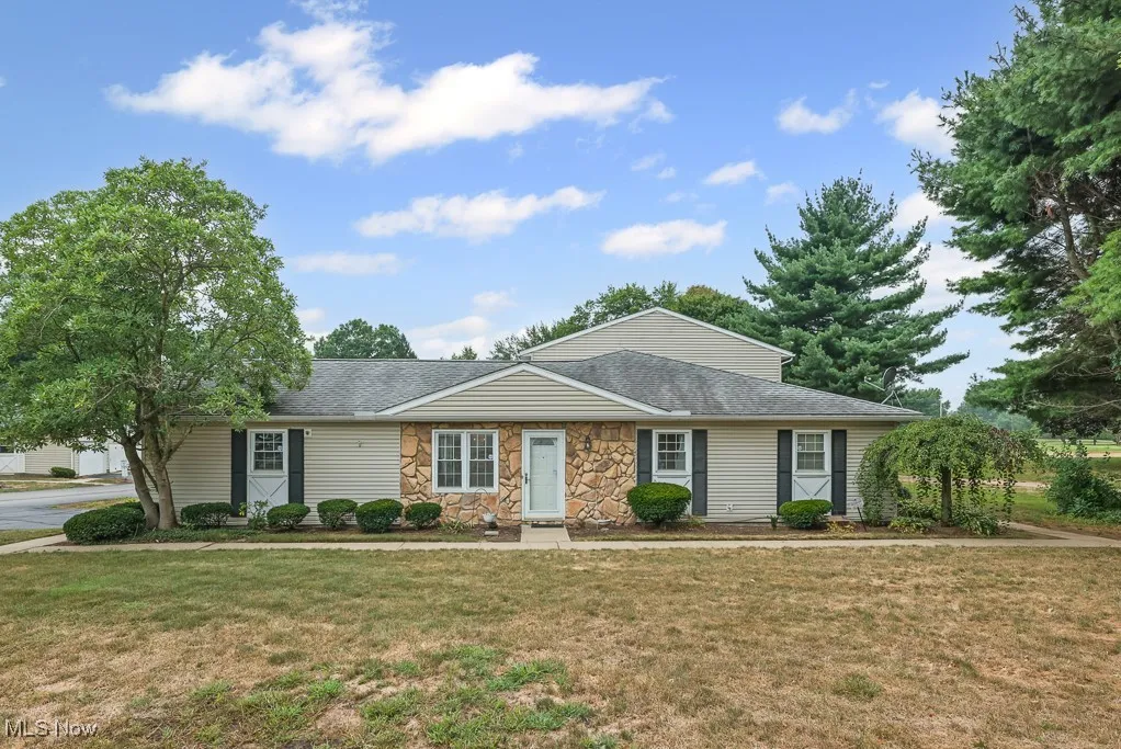 Ranch-style home featuring stone siding, a front yard, and roof with shingles
