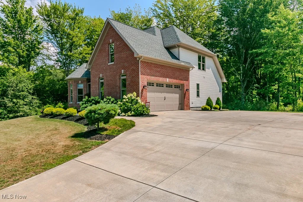 View of property exterior featuring brick siding, concrete driveway, a shingled roof, a yard, and view of wooded area