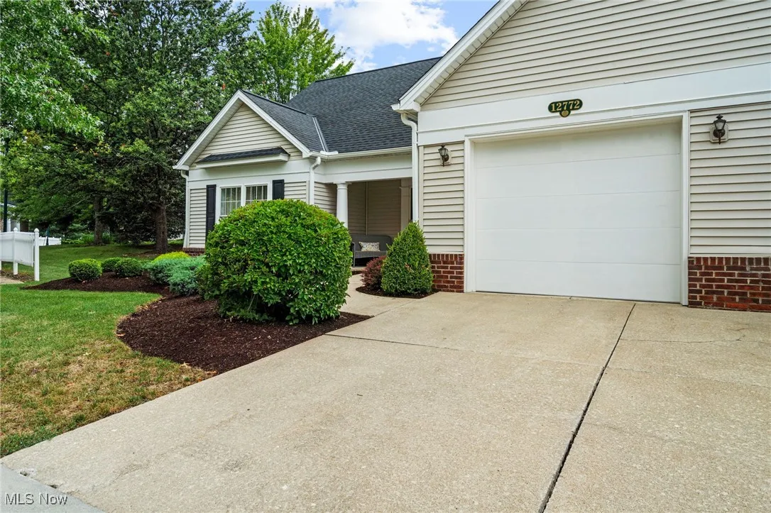 View of front of house with driveway, a garage, a shingled roof, a front yard, and brick siding
