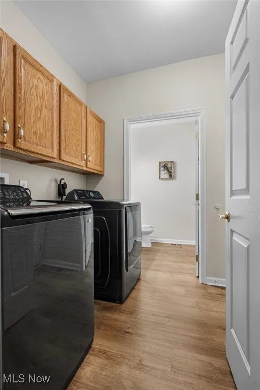 Washroom featuring light wood-type flooring, washing machine and clothes dryer, and cabinet space
