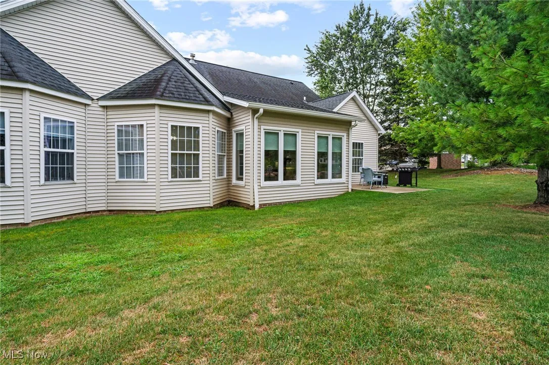 Rear view of house with a yard, a shingled roof, and a patio area
