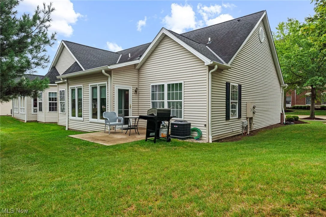 Rear view of property featuring a shingled roof, a yard, and a patio