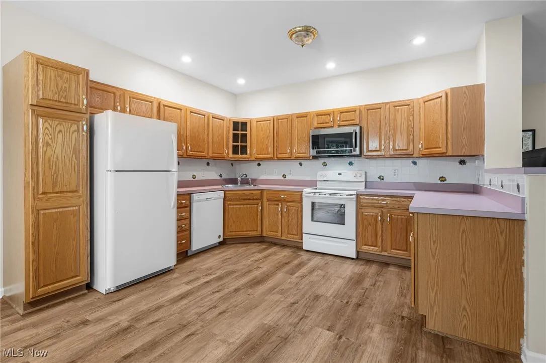 Kitchen with white appliances, light wood finished floors, light countertops, tasteful backsplash, and recessed lighting