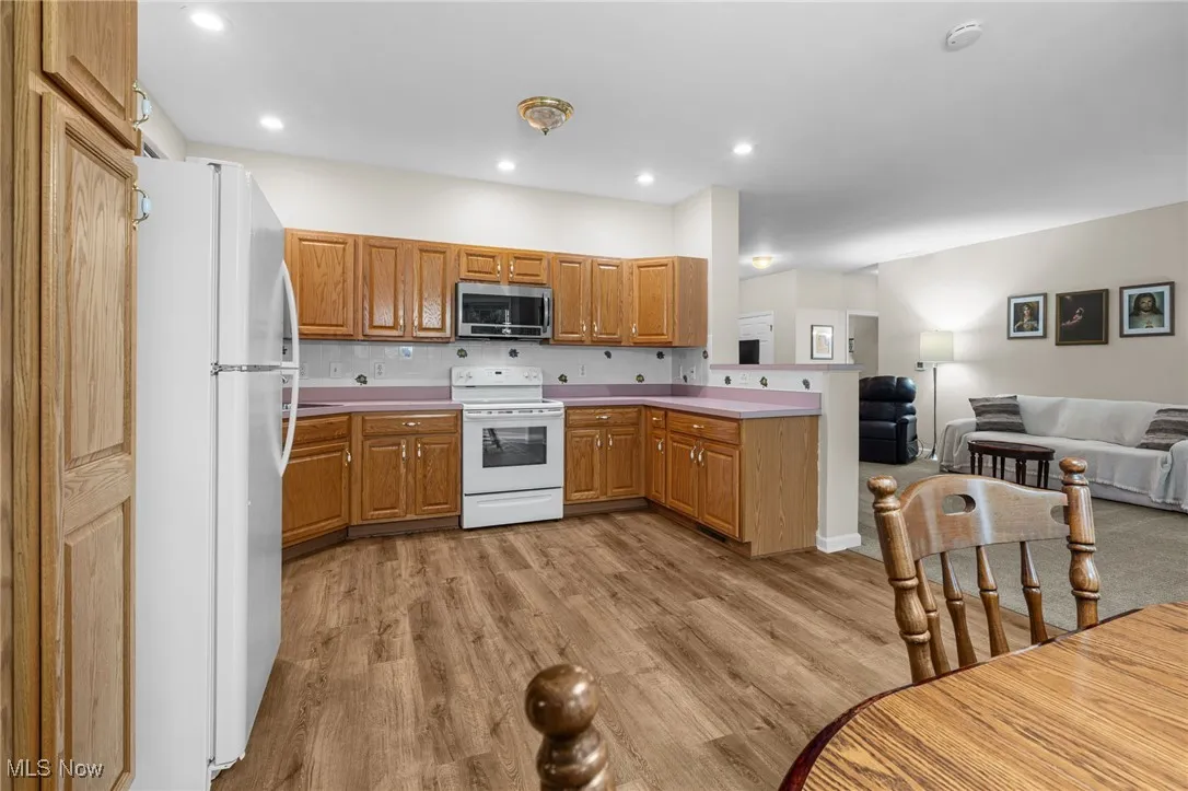Kitchen with backsplash, white appliances, light wood-type flooring, a peninsula, and light countertops