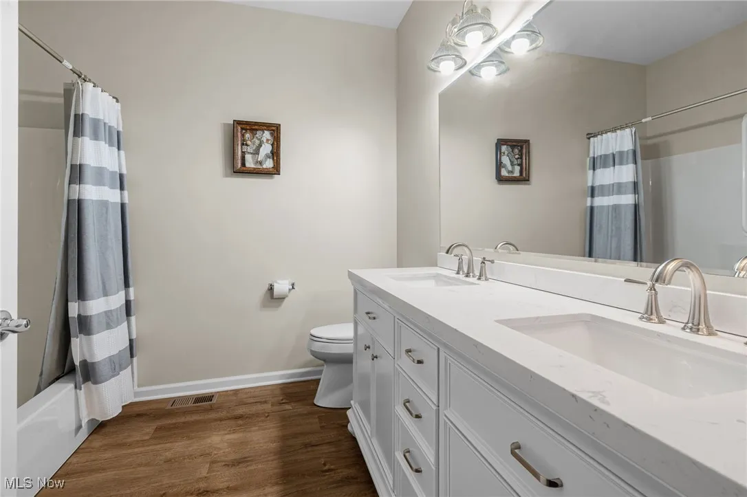 Full bathroom featuring shower / tub combo with curtain, dark wood-style flooring, and double vanity