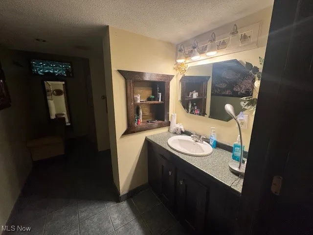 Bathroom with a textured ceiling, vanity, and dark tile patterned flooring