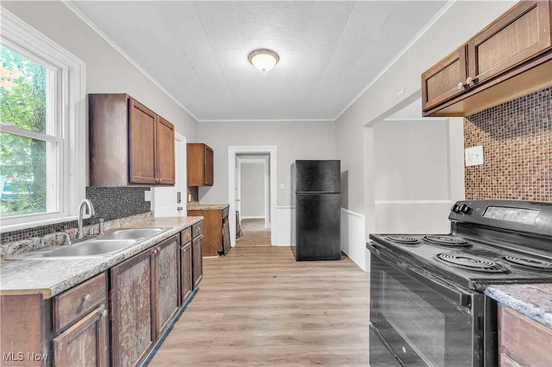 Kitchen featuring decorative backsplash, black appliances, ornamental molding, brown cabinets, and light countertops