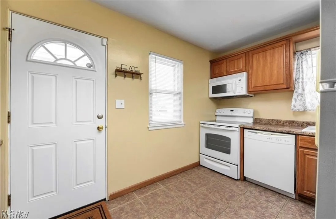 Kitchen featuring white appliances, brown cabinetry, dark tile patterned floors, and dark countertops