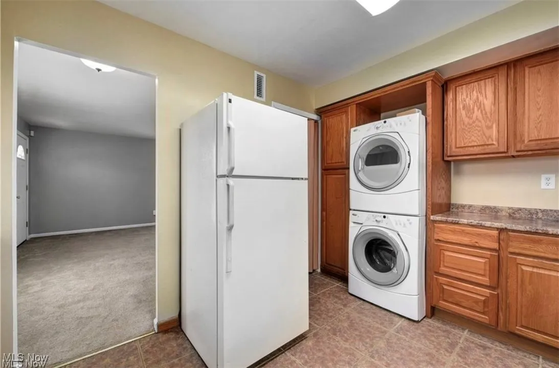 Laundry area with stacked washer and clothes dryer, dark colored carpet, and dark tile patterned flooring