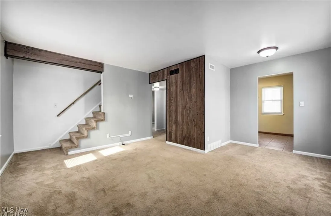 Unfurnished living room with stairs and carpet floors