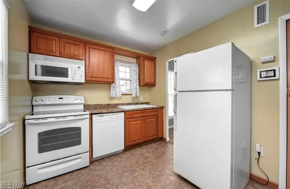 Kitchen featuring white appliances, brown cabinetry, and light tile patterned floors