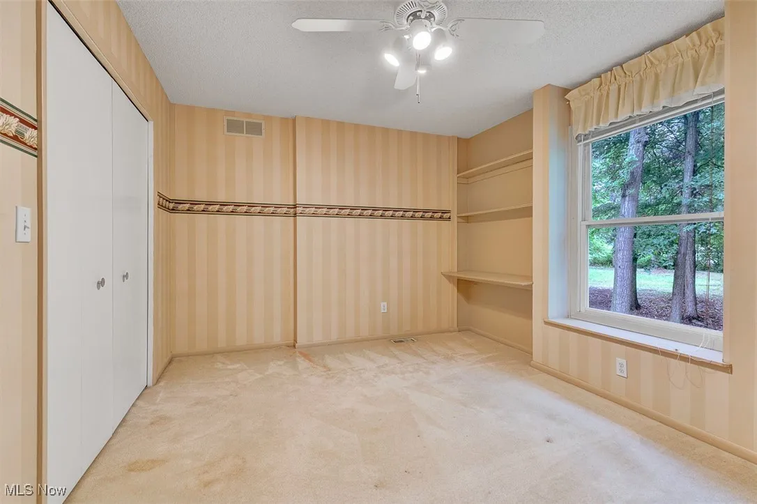 Unfurnished bedroom featuring light carpet, a closet, a textured ceiling, ceiling fan, and wallpapered walls