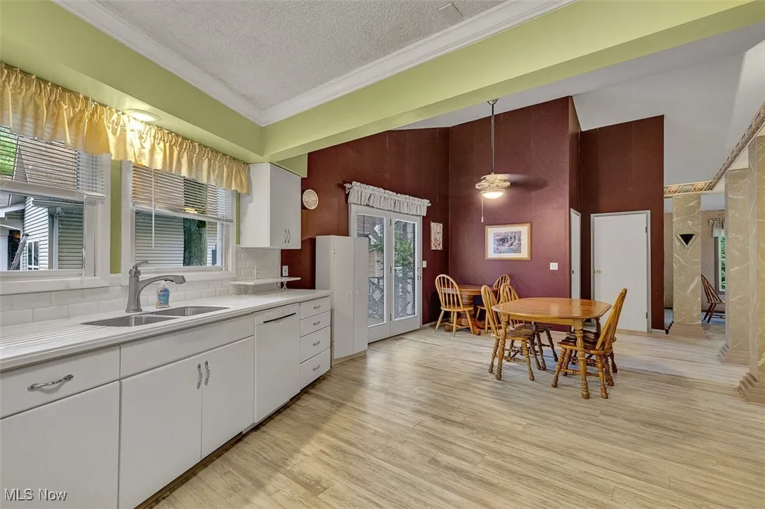 Kitchen featuring light countertops, white cabinetry, ornamental molding, light wood-type flooring, and a textured ceiling