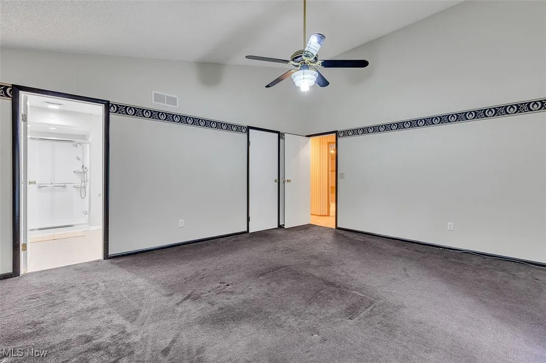 Unfurnished bedroom featuring lofted ceiling, carpet, a ceiling fan, and connected bathroom