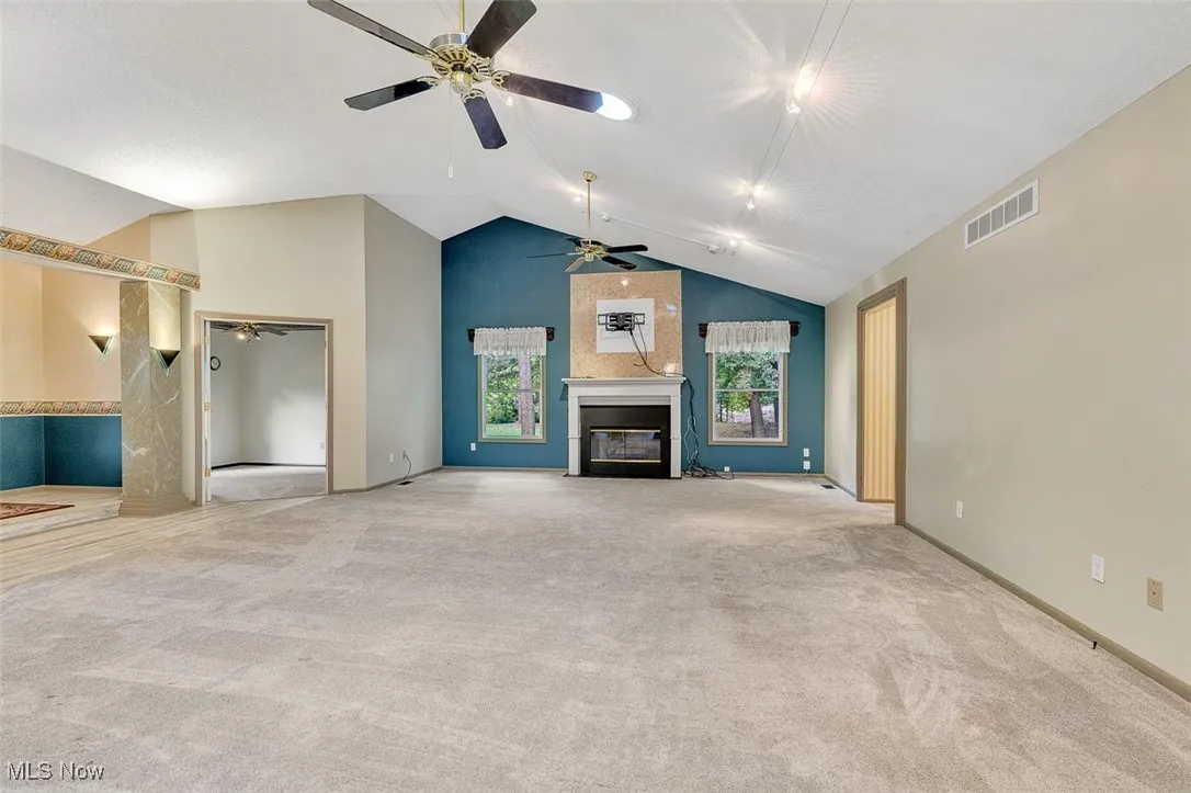 Unfurnished living room with a glass covered fireplace, high vaulted ceiling, light colored carpet, and ceiling fan