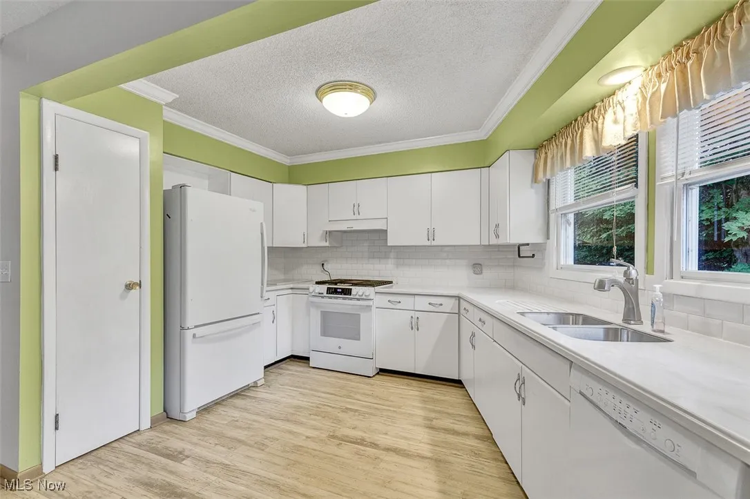 Kitchen featuring light countertops, a textured ceiling, white appliances, white cabinets, and light wood-style floors