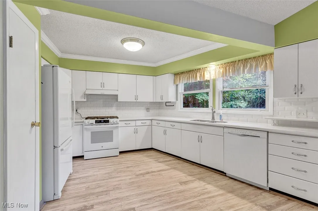 Kitchen featuring a textured ceiling, white appliances, light countertops, white cabinets, and light wood-style flooring