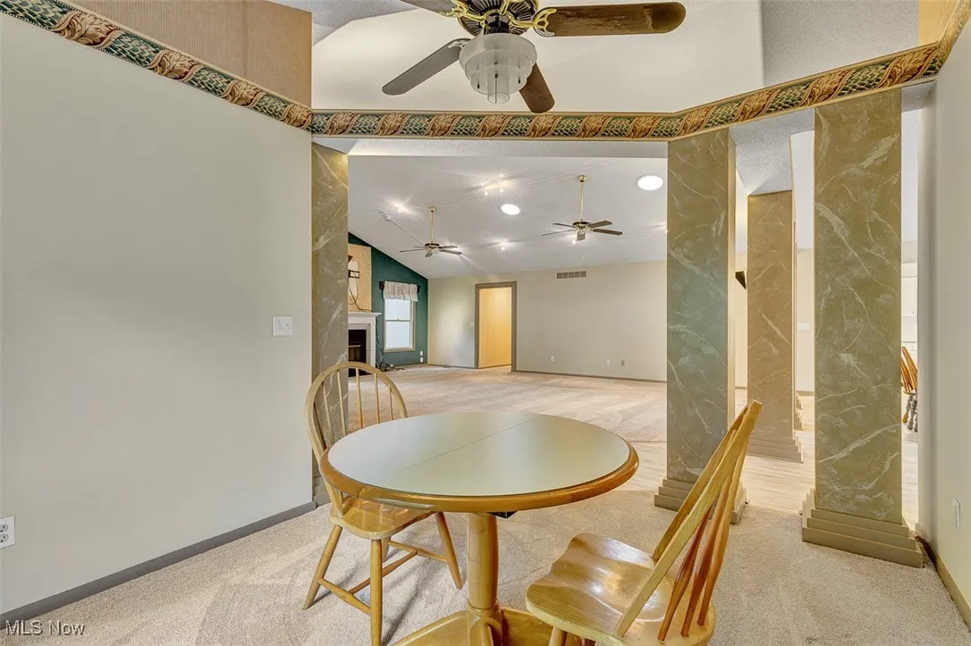 Dining space with light colored carpet, a fireplace, and vaulted ceiling