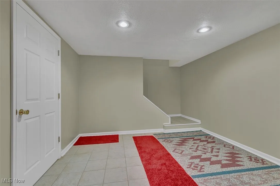 Finished below grade area featuring a textured ceiling, light tile patterned flooring, and recessed lighting
