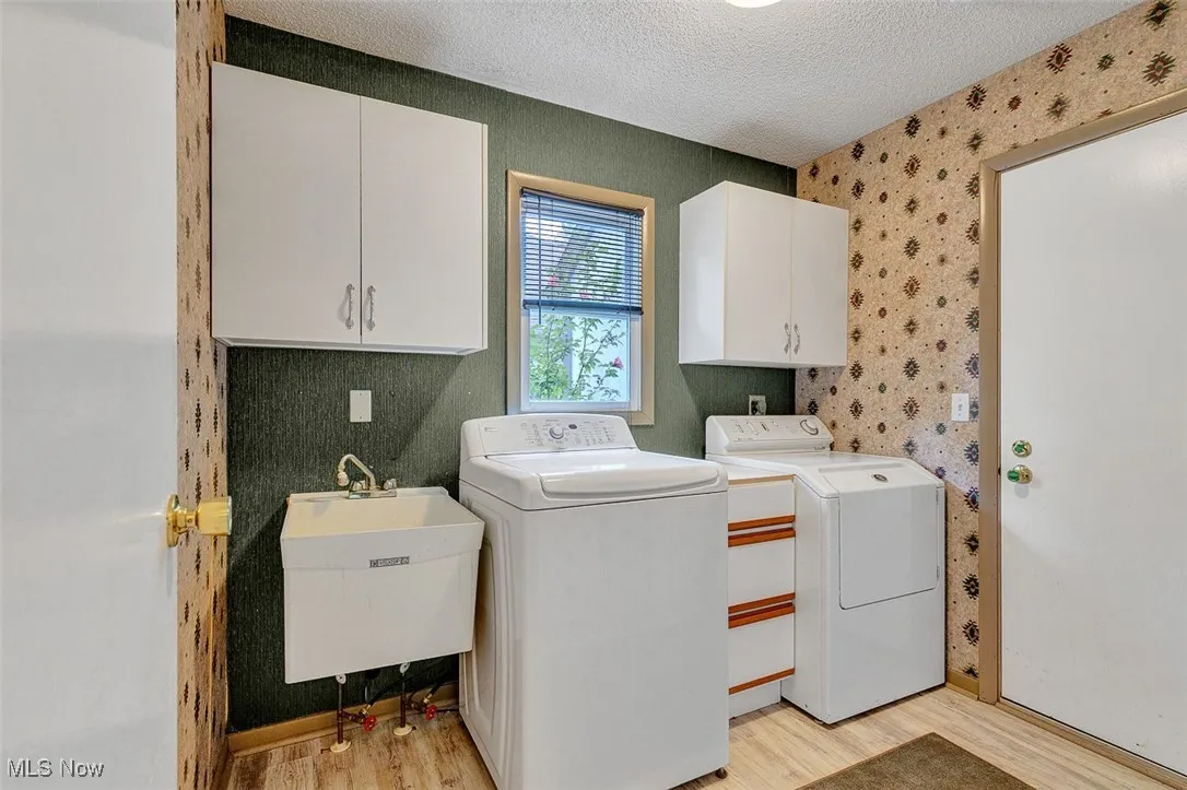 Laundry room featuring a textured ceiling, cabinet space, light wood-type flooring, wallpapered walls, and washing machine and clothes dryer