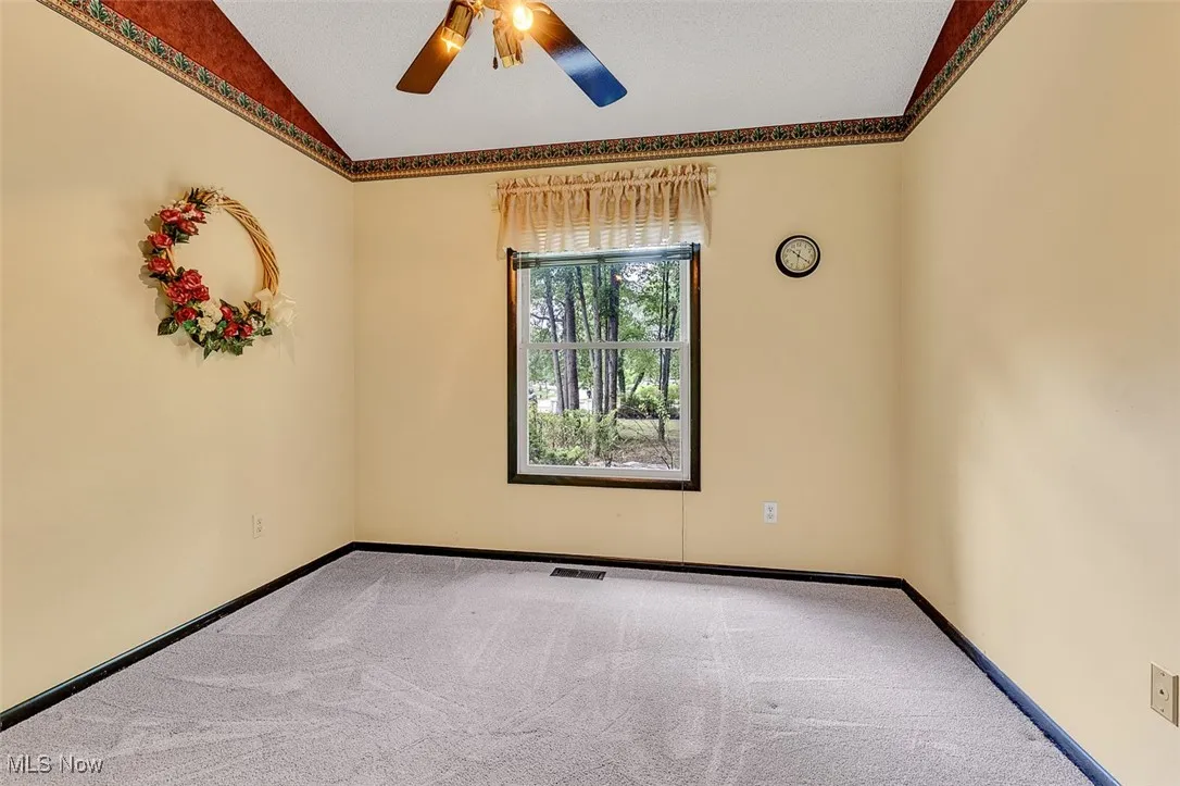 Spare room featuring carpet flooring, vaulted ceiling, and ceiling fan