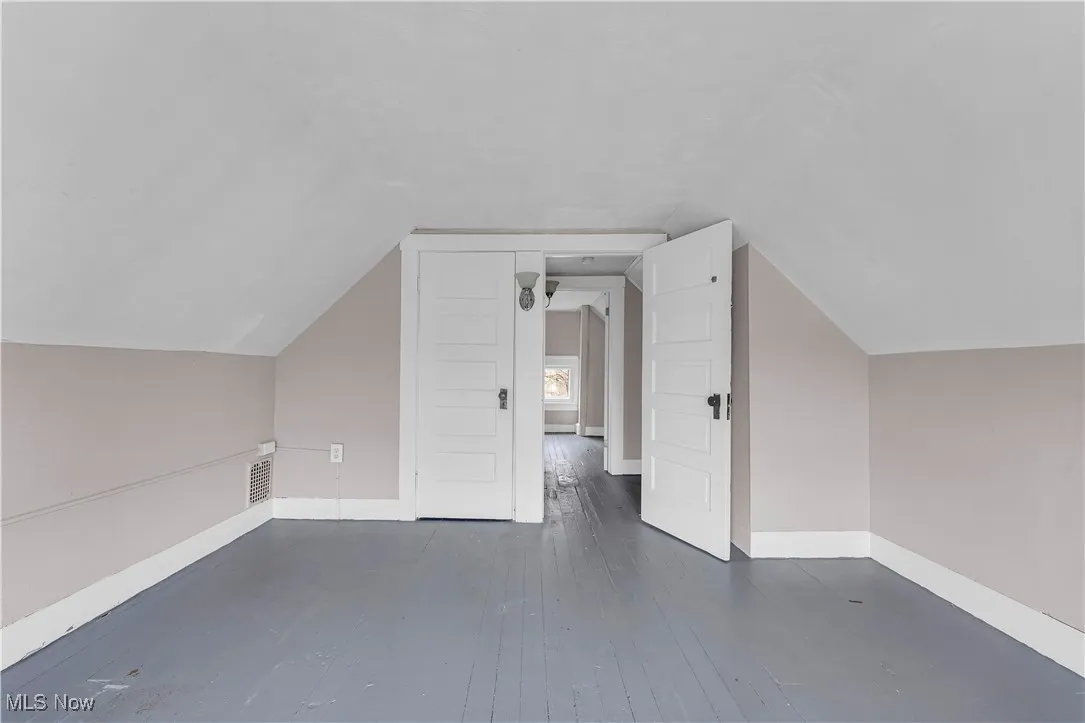 Bonus room with dark wood-style floors and vaulted ceiling