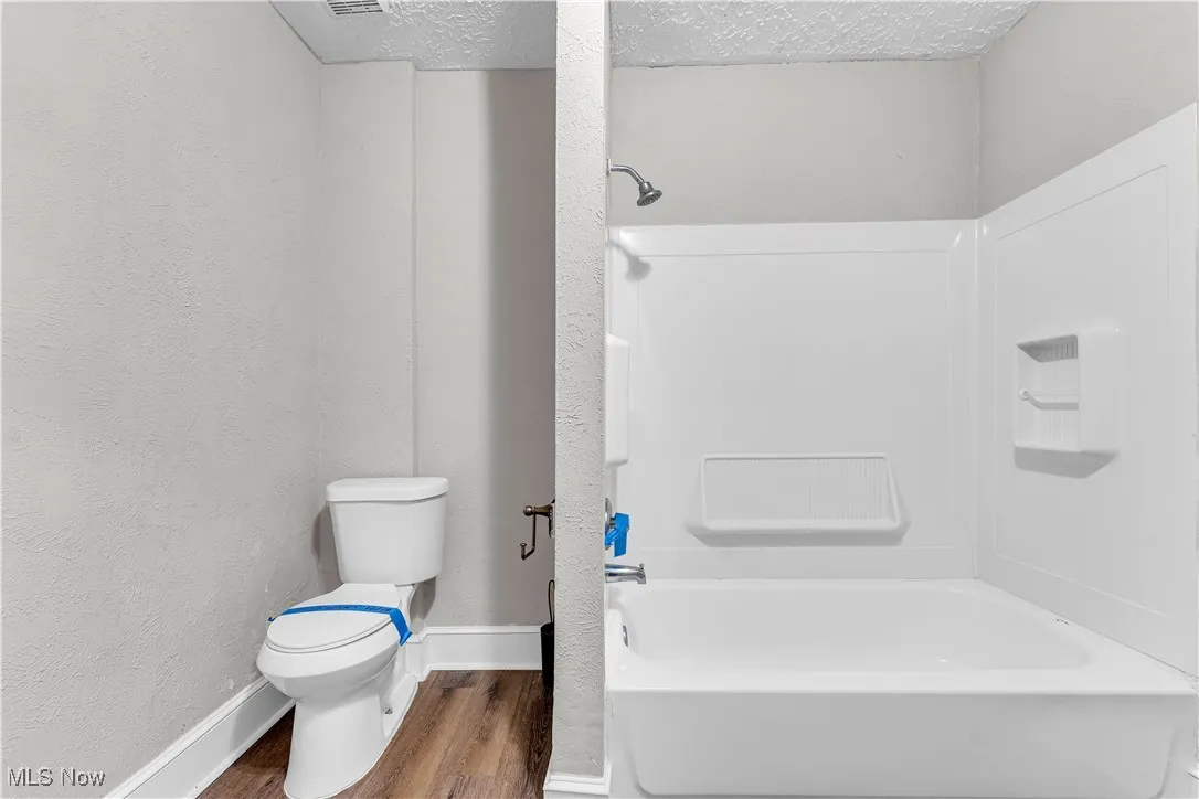 Full bath with shower / bath combination, wood finished floors, a textured wall, and a textured ceiling
