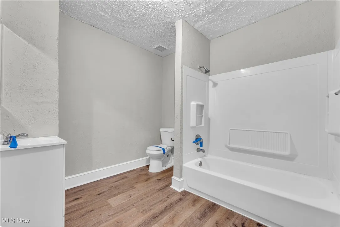 Bathroom with tub / shower combination, a textured ceiling, light wood-type flooring, vanity, and a textured wall