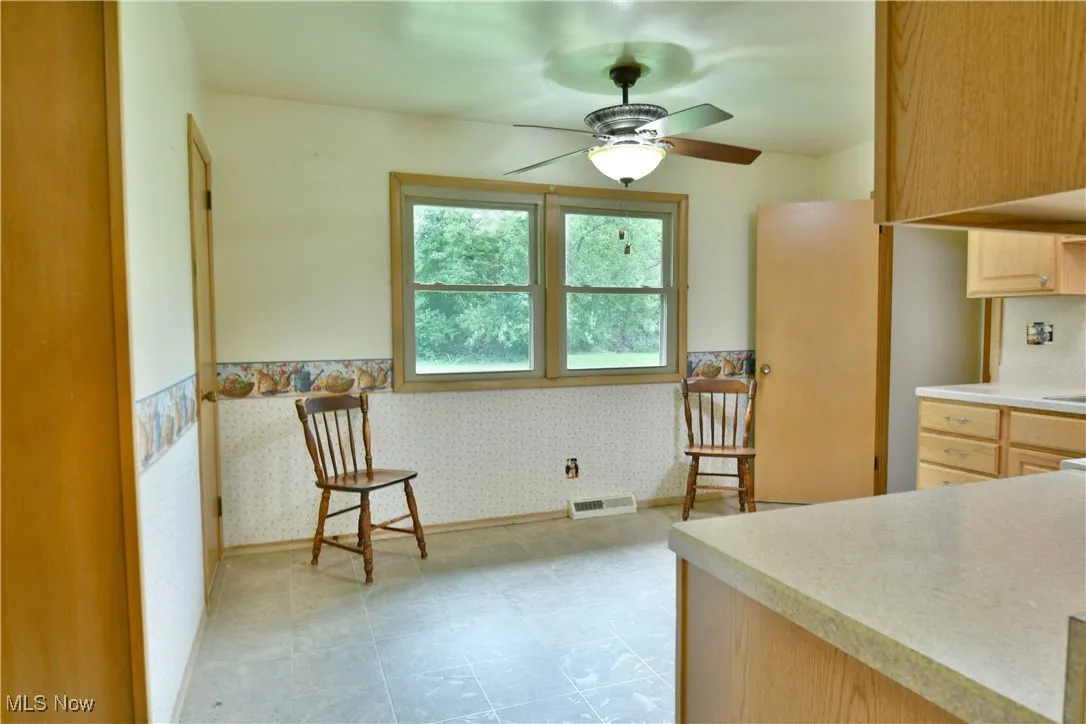 Kitchen with wallpapered walls, a wainscoted wall, light brown cabinets, and ceiling fan