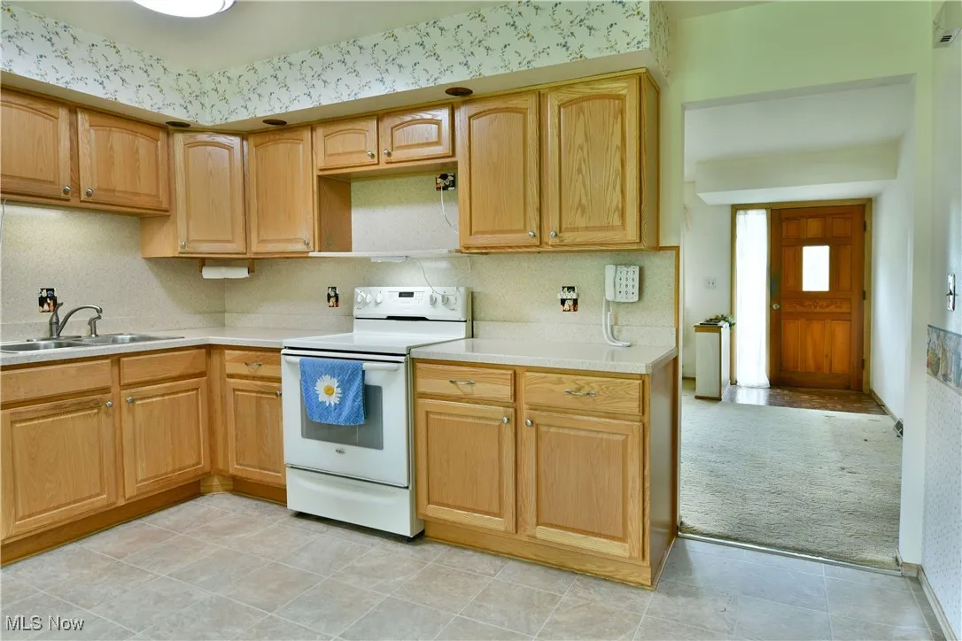 Kitchen with white electric stove, light countertops, light carpet, decorative backsplash, and light tile patterned floors