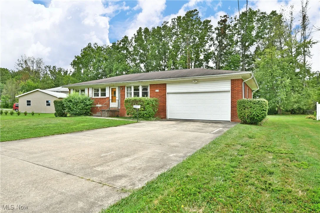 Single story home with an attached garage, brick siding, a front yard, concrete driveway, and view of scattered trees