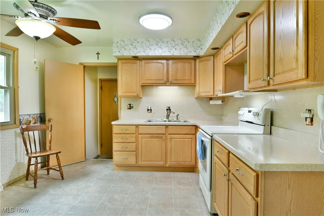 Kitchen featuring electric range, light countertops, light brown cabinetry, and ceiling fan