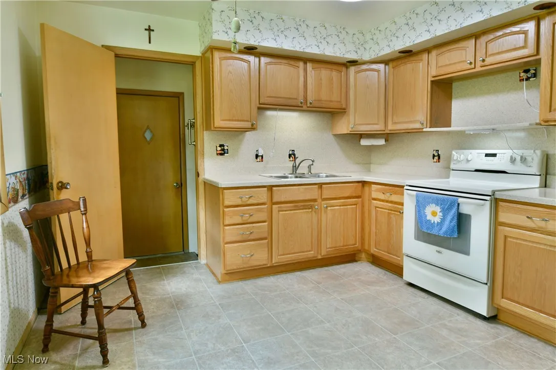 Kitchen featuring white range with electric stovetop, light countertops, light brown cabinetry, and tasteful backsplash