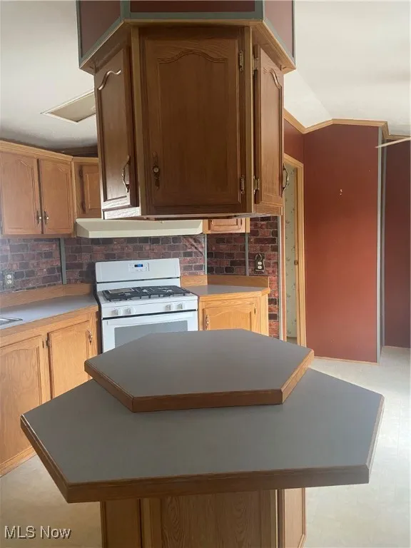 Kitchen with stove, light floors, backsplash, light countertops, and crown molding
