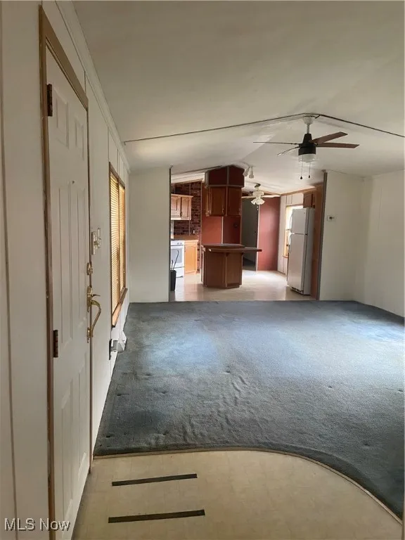 Unfurnished living room with light carpet, ceiling fan, and vaulted ceiling
