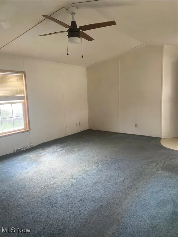 Carpeted spare room featuring vaulted ceiling, ornamental molding, and a ceiling fan
