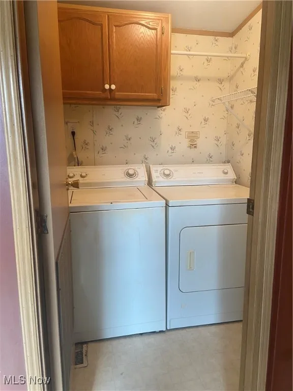 Laundry area with wallpapered walls, cabinet space, light flooring, and washing machine and dryer