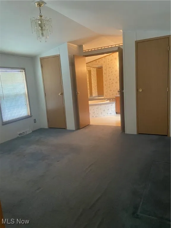 Unfurnished bedroom with wallpapered walls, carpet floors, lofted ceiling, and a chandelier