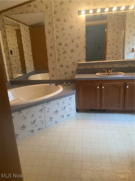 Bathroom with wallpapered walls, vanity, a bath, and light tile patterned floors