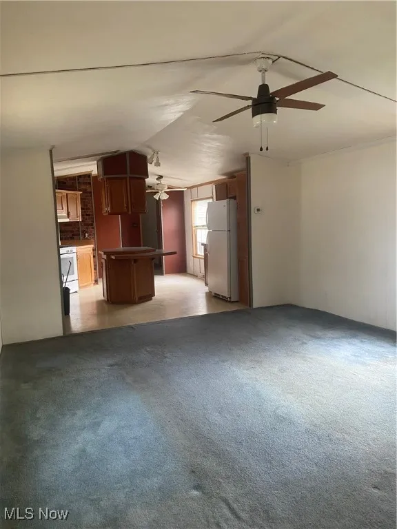 Unfurnished living room with ceiling fan, vaulted ceiling, and light colored carpet