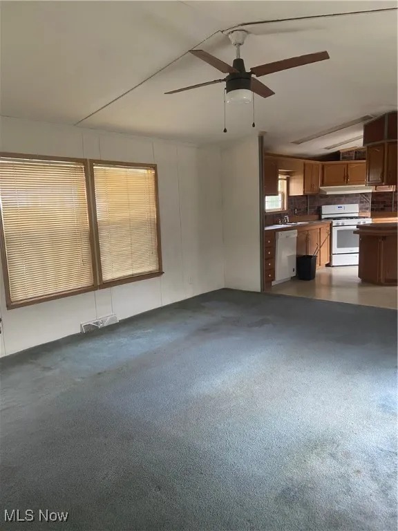 Unfurnished living room featuring a ceiling fan and carpet flooring