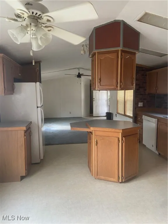 Kitchen featuring lofted ceiling, fridge, brown cabinets, a ceiling fan, and dishwashing machine