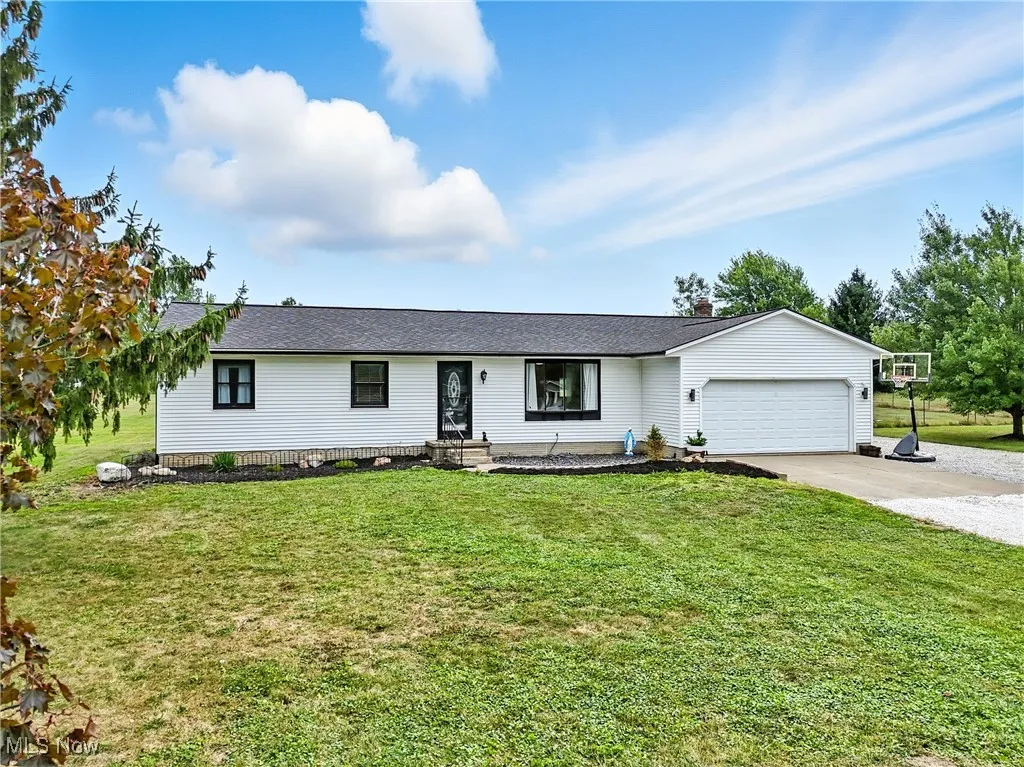 Ranch-style home with driveway, an attached garage, a front lawn, roof with shingles, and a chimney