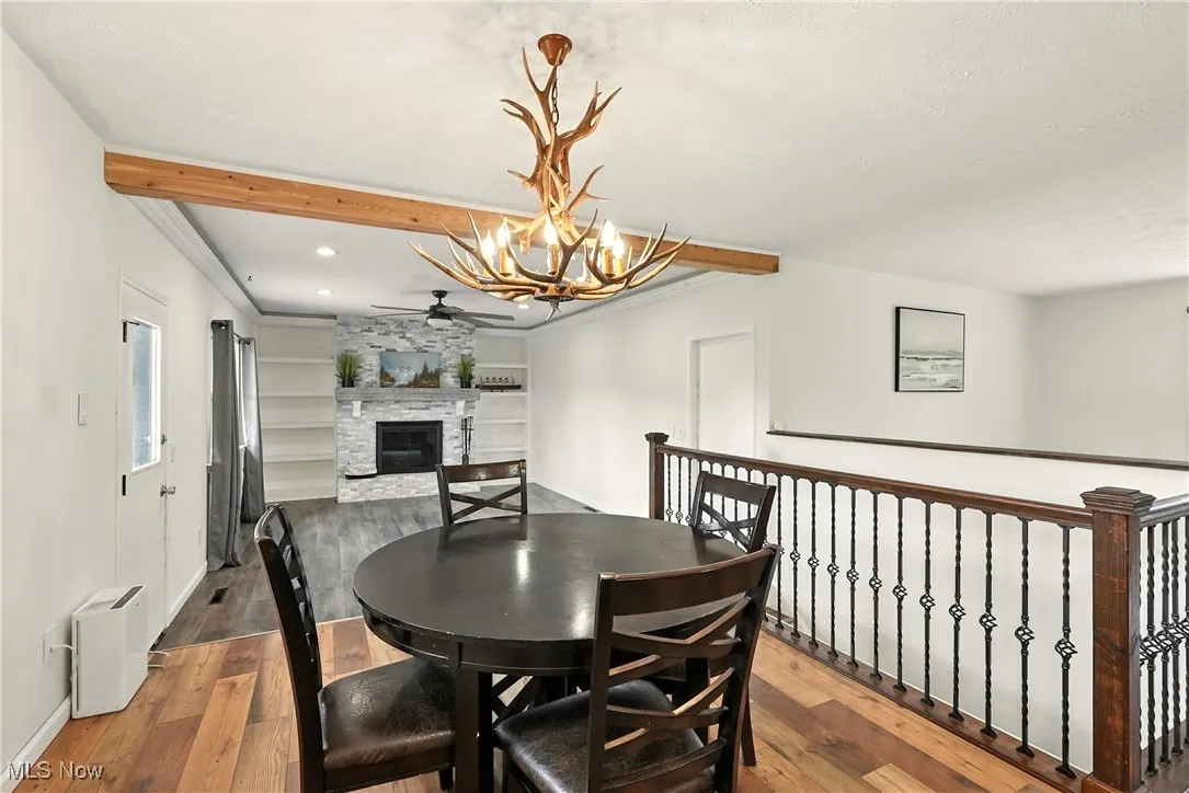 Dining space featuring beamed ceiling, a stone fireplace, hardwood / wood-style flooring, a chandelier, and crown molding