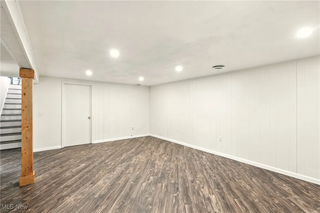 Finished basement with dark wood-type flooring, stairway, recessed lighting, and wood walls