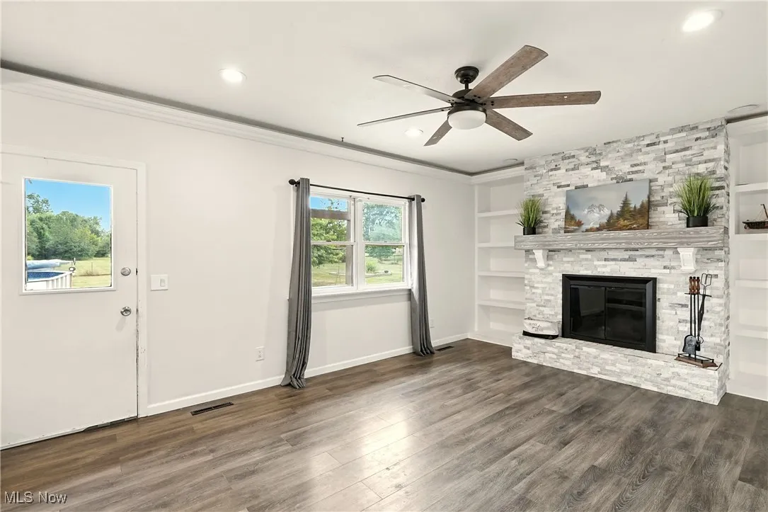 Unfurnished living room featuring dark wood-style flooring, built in features, a stone fireplace, a ceiling fan, and recessed lighting